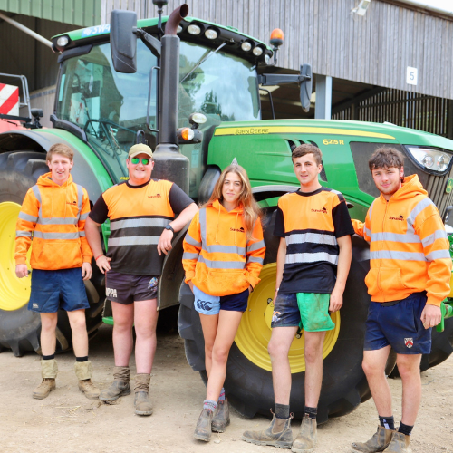 five people in orange vests stand in front of a green trctor