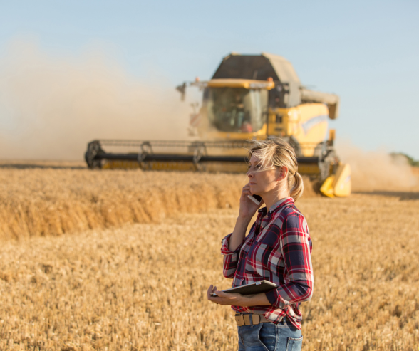 woman stands in a part-harvested field with a combine harvester behind her